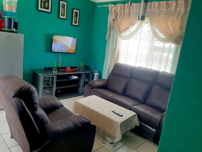 A living room featuring tiled flooring and a window fitted with security bars and curtain rails.