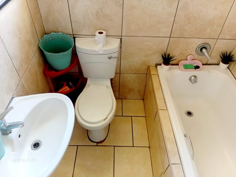A compact bathroom featuring a standard toilet, pedestal basin, and a built-in bathtub with tiled surrounds and flooring.