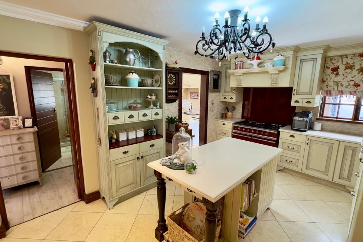 A traditional-style kitchen featuring custom cabinetry, a central island, a built-in range with a red splashback, and a decorative chandelier.