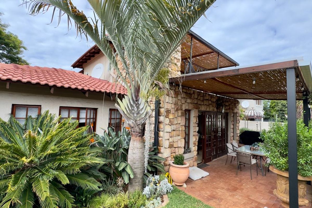 A charming rear patio area featuring natural stone cladding, a covered pergola structure, and terracotta tiled flooring, overlooking a lush garden.