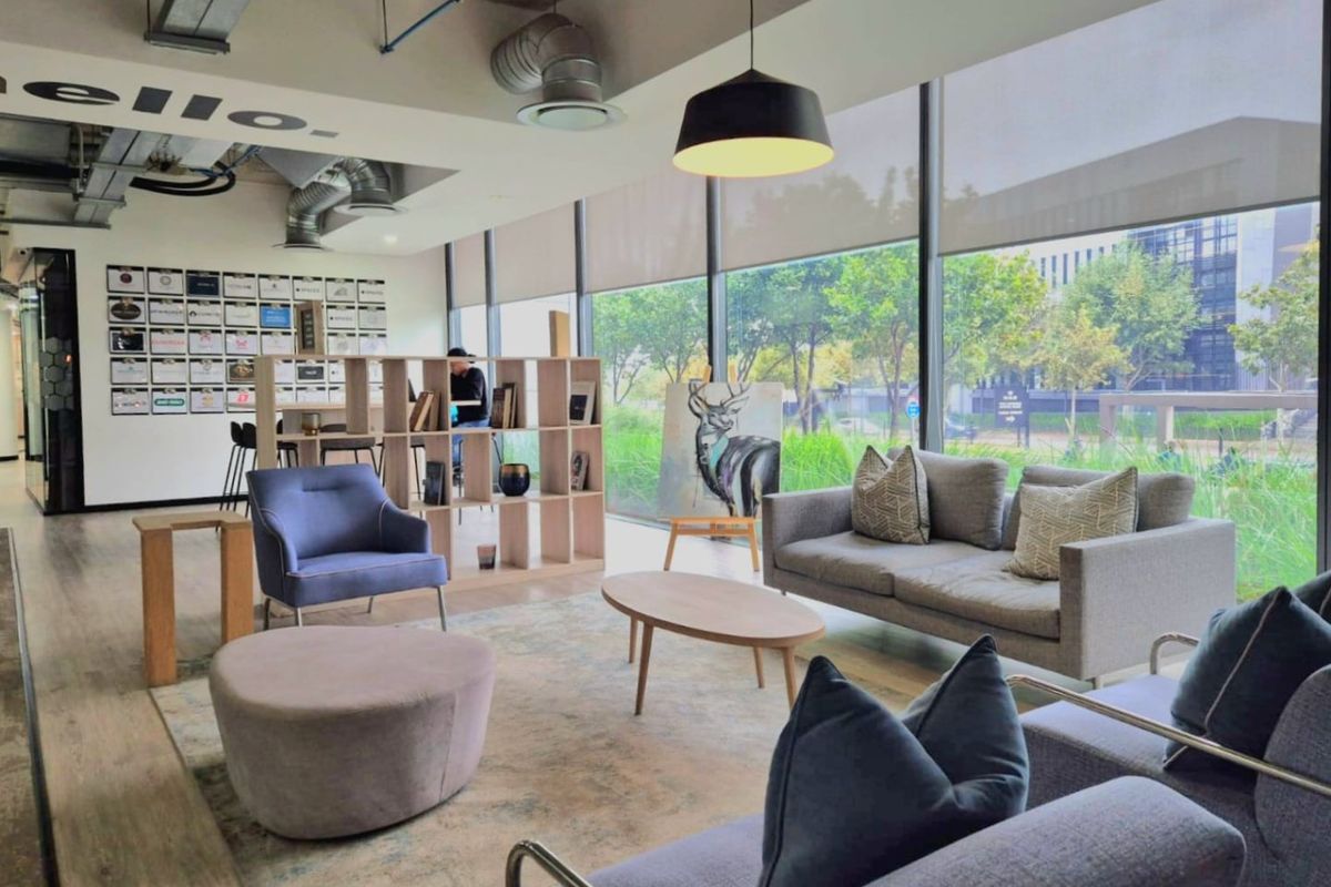 Modern commercial lounge area featuring exposed industrial ceiling ducting, expansive floor-to-ceiling windows with roller blinds, and durable laminate flooring.