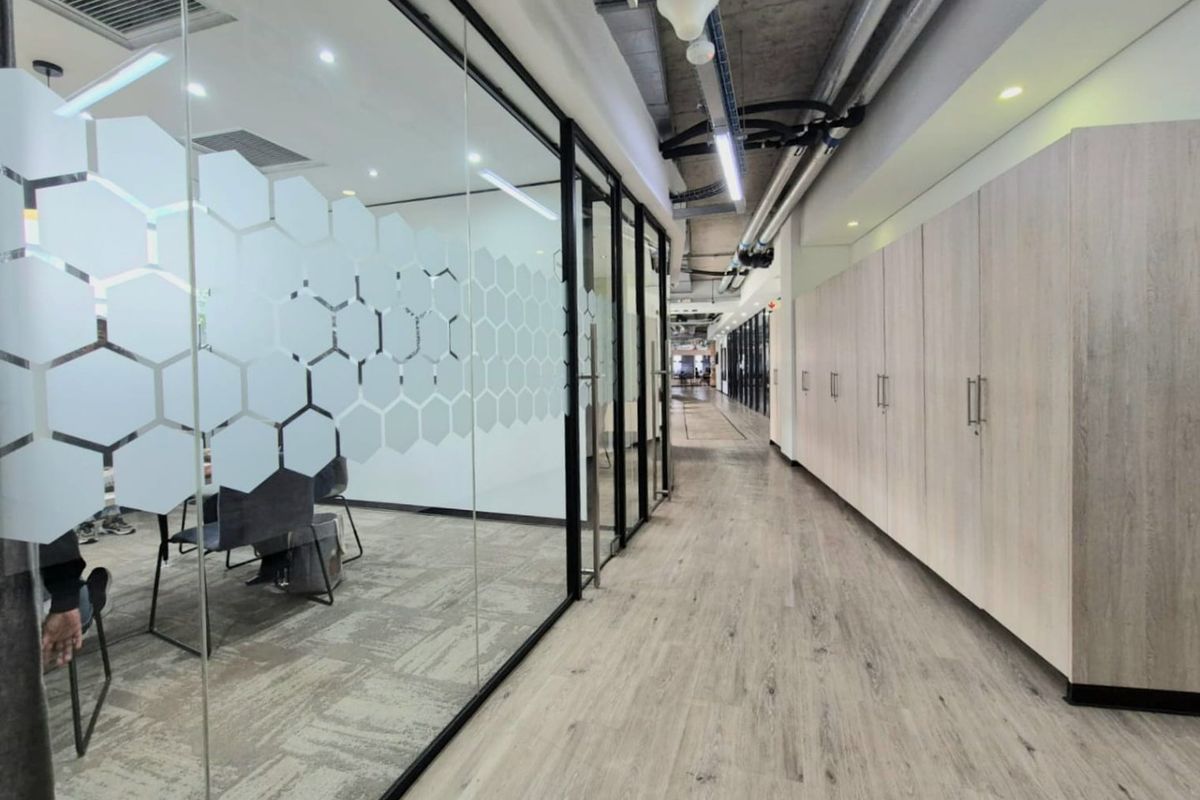 Modern commercial office hallway featuring glass-partitioned meeting rooms, extensive built-in storage cabinetry, and an industrial-style exposed ceiling with integrated lighting.