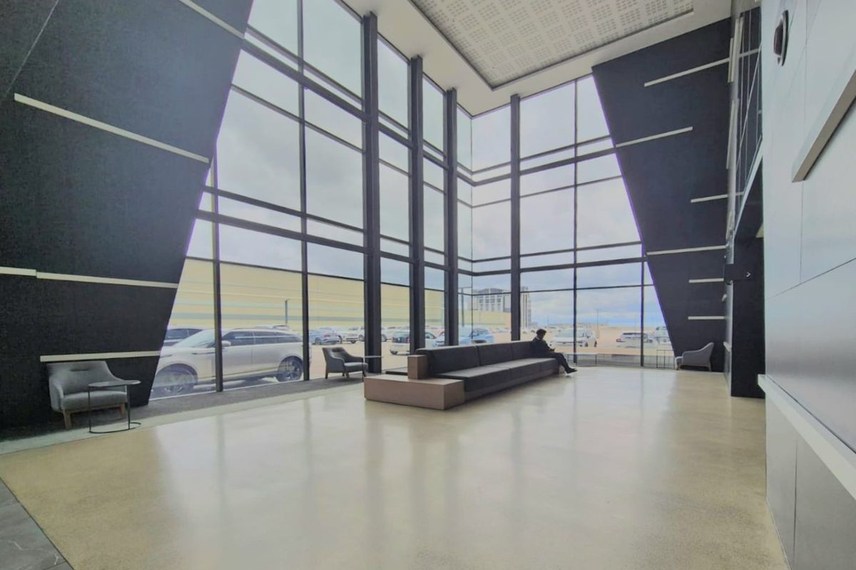Spacious commercial entrance lobby featuring double-volume floor-to-ceiling glass windows, polished concrete floors, and modern architectural design elements.