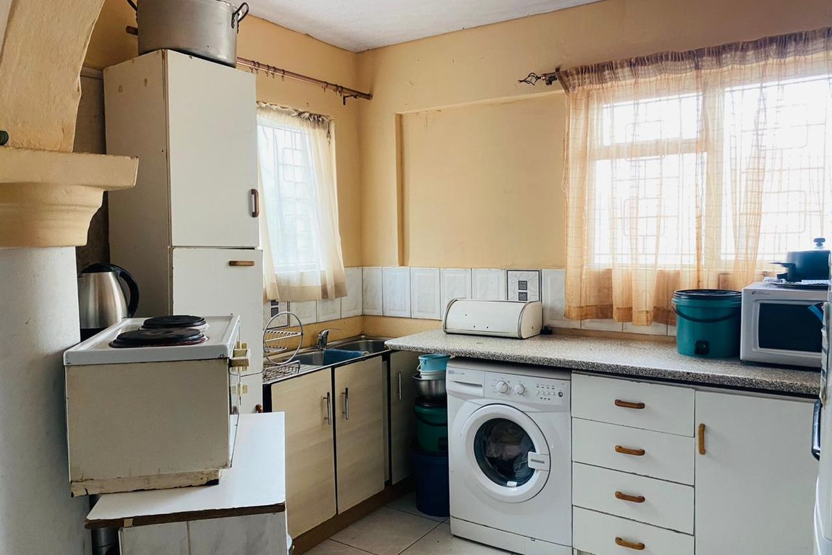 A compact, dated kitchen featuring built-in cabinetry, laminate countertops, tiled backsplash, and integrated laundry plumbing, offering potential for a modern renovation.