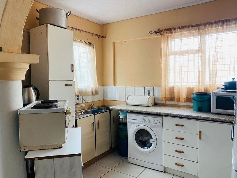 A compact, dated kitchen featuring built-in cabinetry, laminate countertops, tiled backsplash, and integrated laundry plumbing, offering potential for a modern renovation.