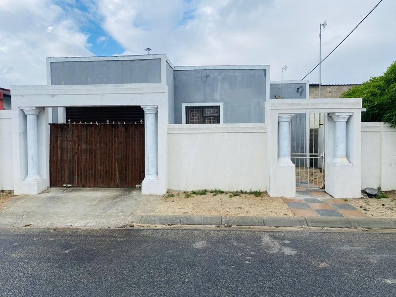 Front elevation of a house featuring a boundary wall, decorative columns, a pedestrian gate, and a driveway gate with a paved entrance path.