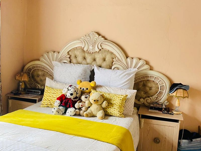 A bedroom featuring a timber ceiling, laminate flooring, and a decorative headboard. The walls show signs of minor plaster cracking.