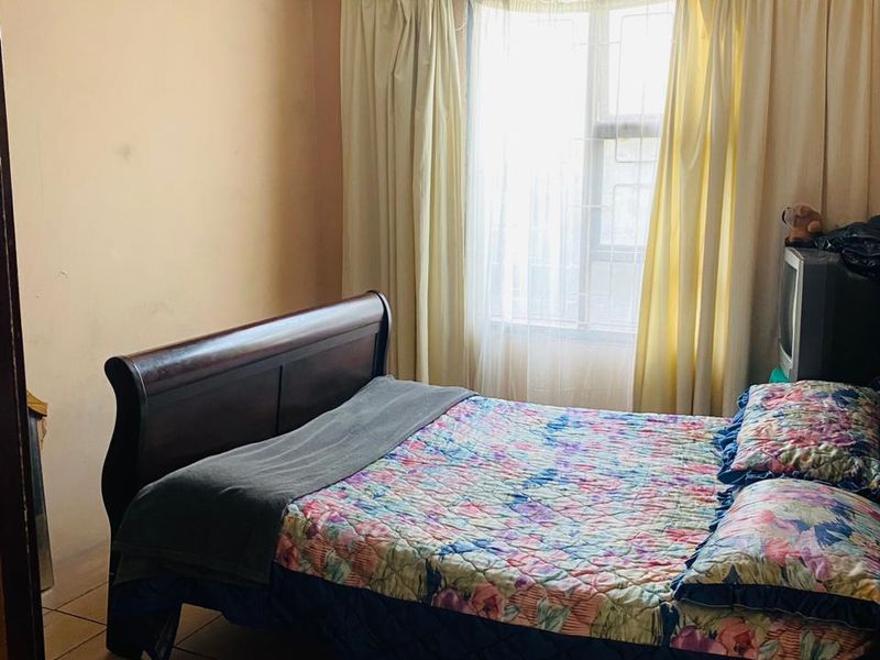 A bedroom featuring wooden flooring and a window with natural light. The walls show signs of wear and require cosmetic attention.
