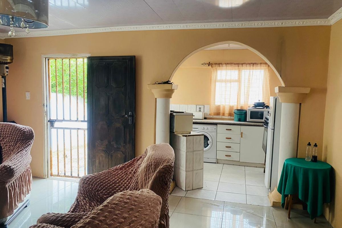 Open-plan living area featuring an arched transition to a functional kitchen with built-in cabinetry and tiled flooring throughout.