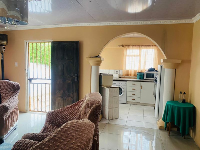 Open-plan living area featuring an arched transition to a functional kitchen with built-in cabinetry and tiled flooring throughout.