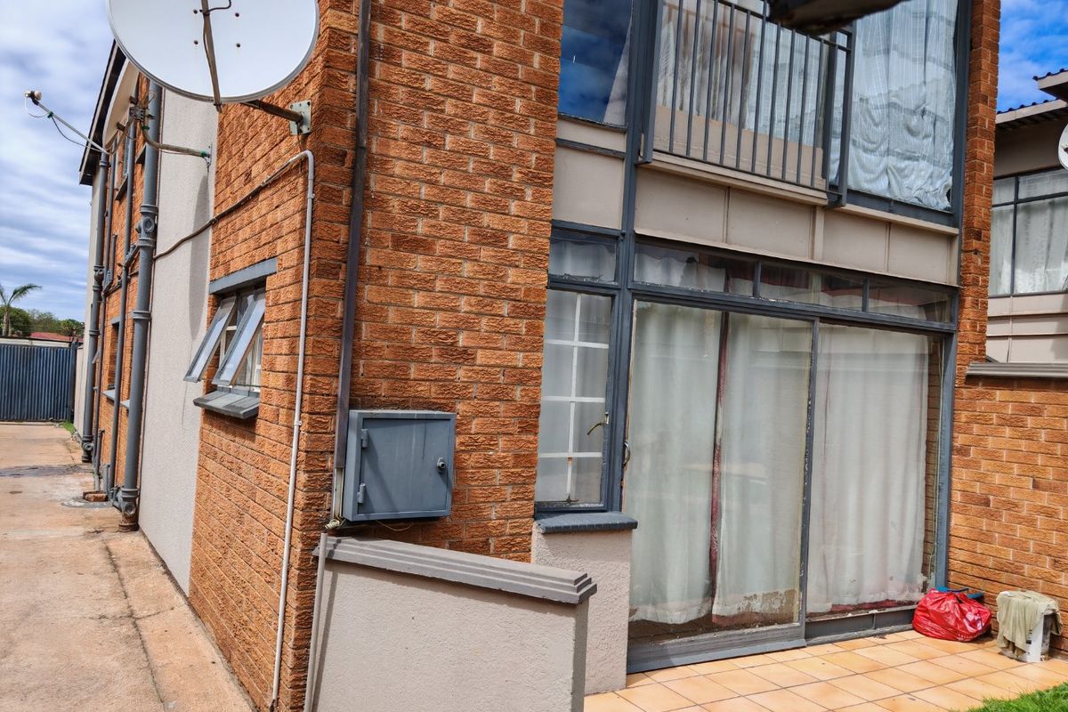 Rear exterior view of a multi-story brick commercial building featuring a tiled patio, sliding glass doors, and a balcony with metal railings.