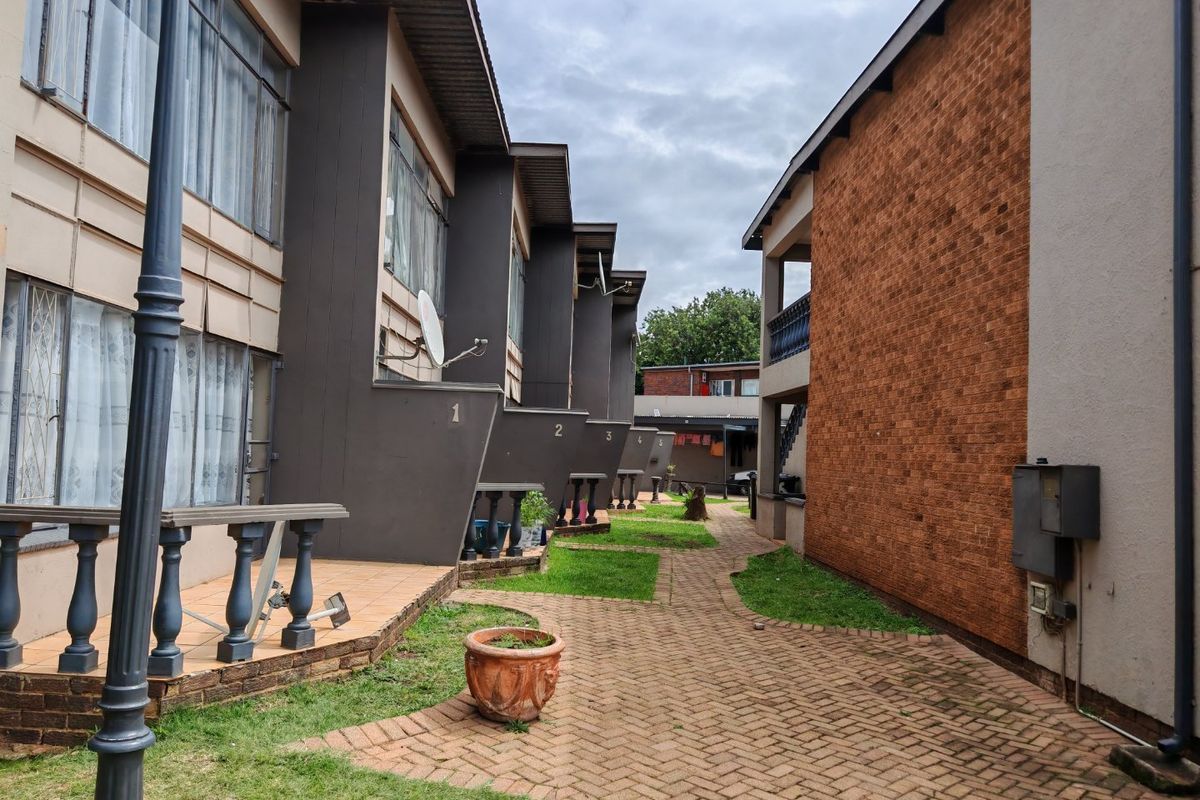A view of the rear exterior of a commercial complex featuring a paved walkway between multi-level units with private patios and brick wall finishes.