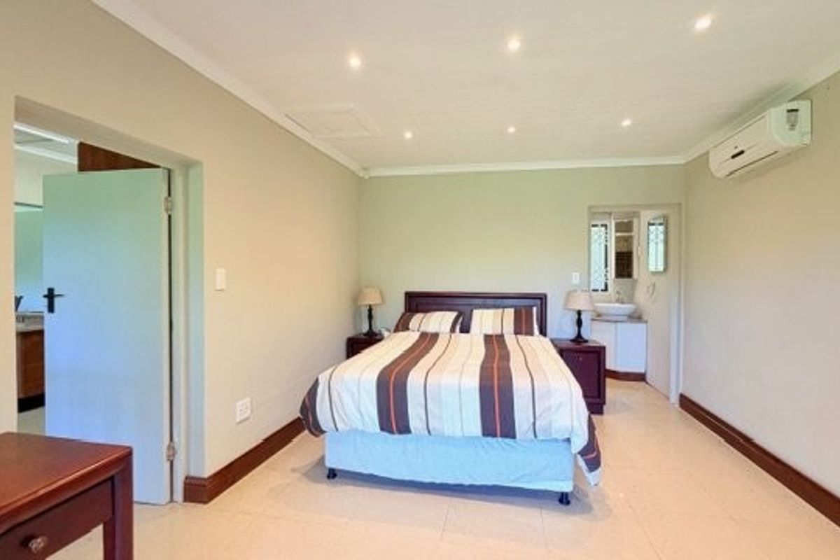 Spacious bedroom featuring tiled flooring, recessed downlighting, a wall-mounted air conditioning unit, and direct access to an en-suite bathroom.