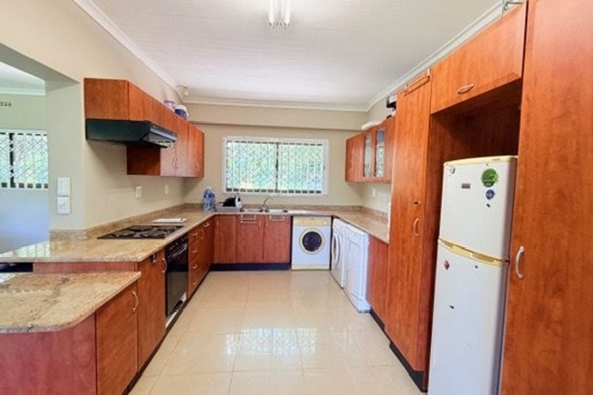 A functional kitchen featuring wood-finish cabinetry, granite countertops, integrated appliances, and tiled flooring with natural light from dual windows.
