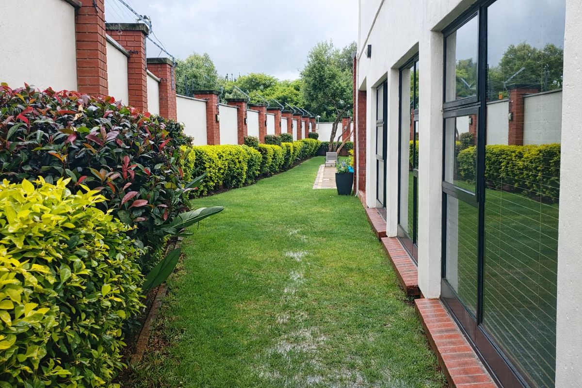 A well-maintained rear garden area featuring a manicured lawn, paved walkway, and a secure brick boundary wall with electric fencing.