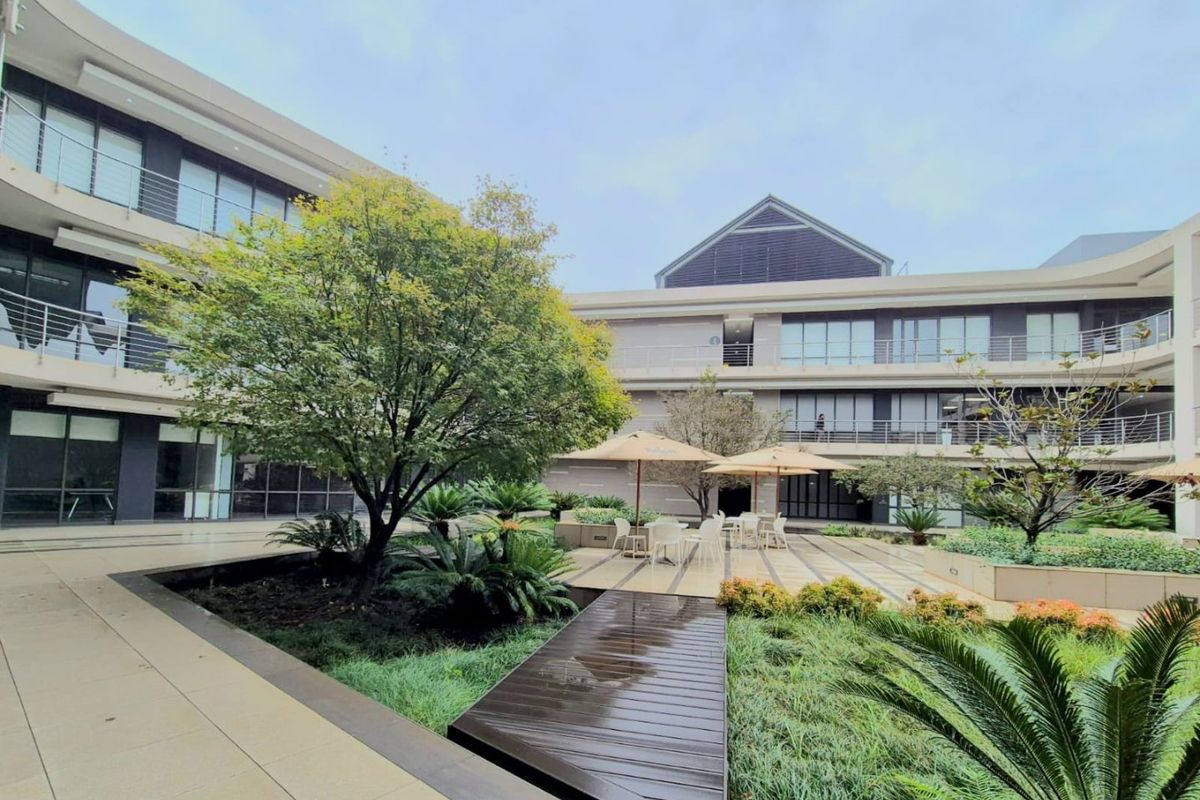 A well-maintained commercial courtyard featuring landscaped gardens, paved walkways, timber decking, and modern multi-story office building facades with glass balustrades.