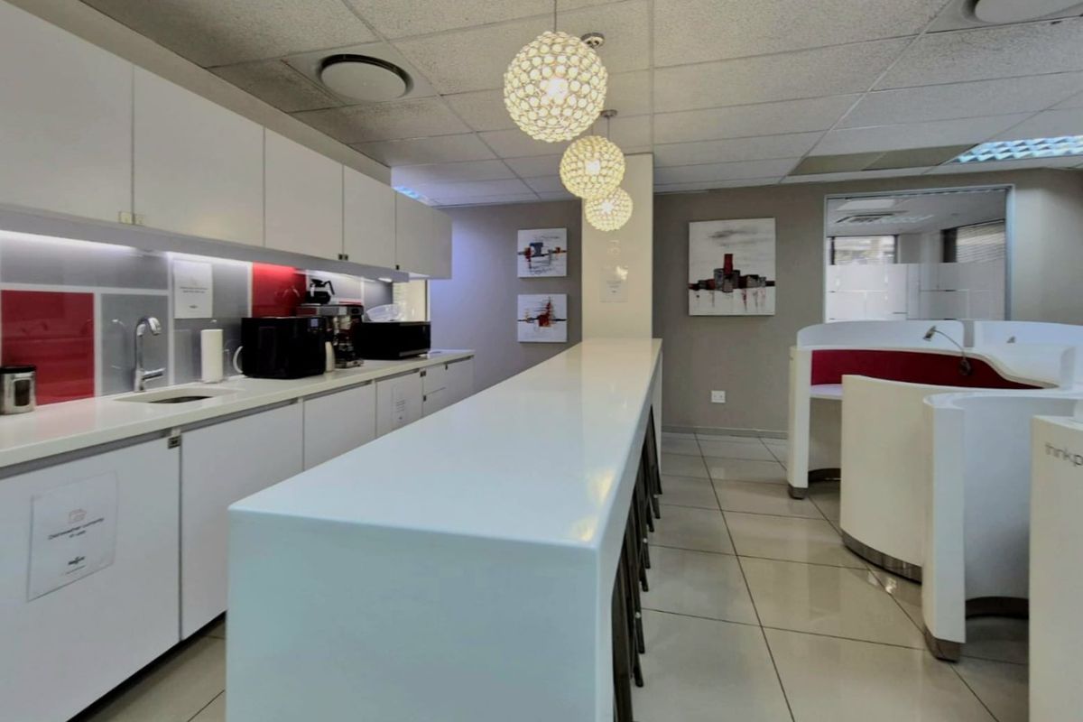 A modern commercial kitchenette featuring white built-in cabinetry, a long breakfast bar, tiled flooring, and contemporary pendant lighting.