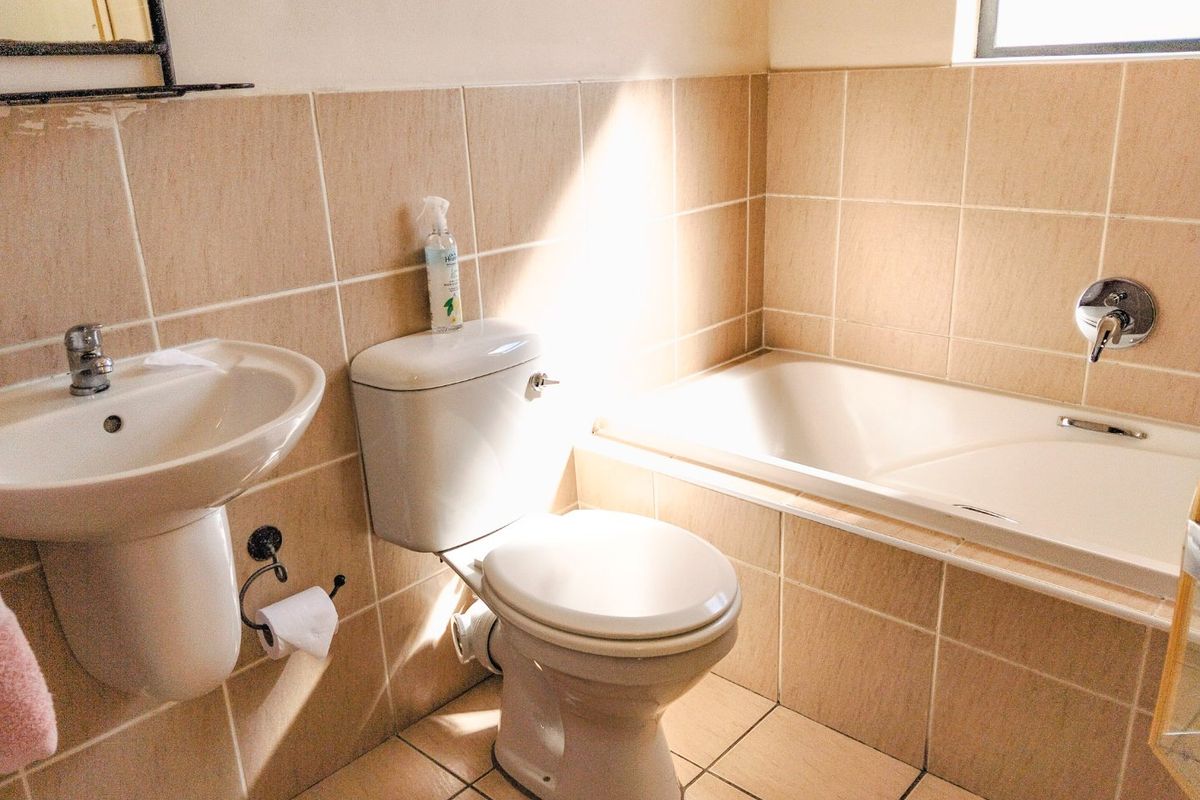 A functional bathroom featuring a pedestal basin, toilet, and a built-in bathtub with neutral ceramic wall and floor tiling.