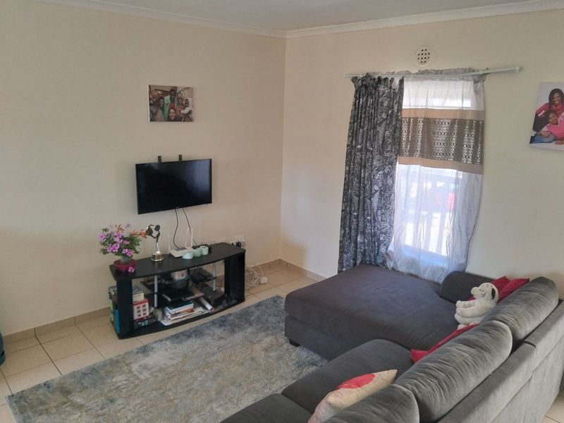 A functional living room featuring tiled flooring, a wall-mounted television bracket, and a window with installed curtain rods.