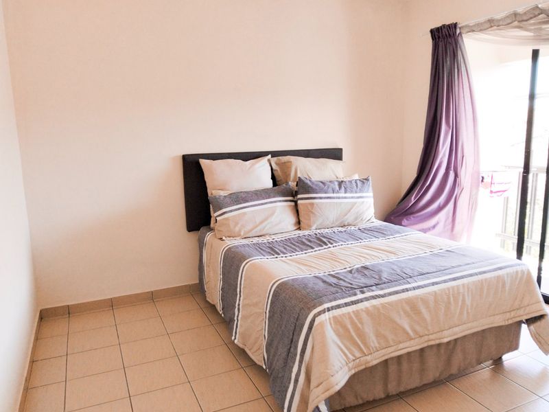 A functional bedroom featuring tiled flooring and a sliding glass door providing natural light and access to an outdoor area.