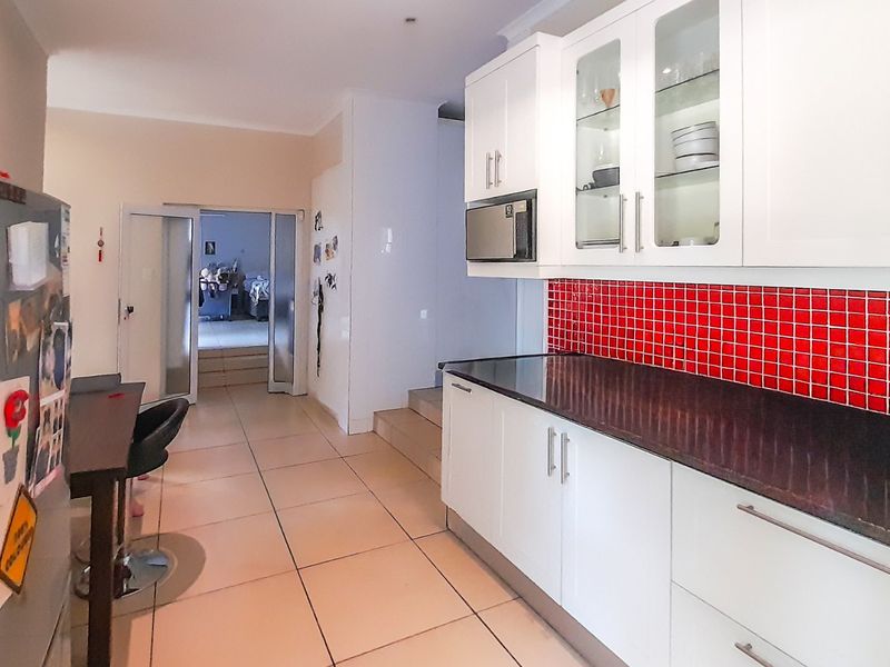 Modern kitchen featuring white cabinetry, dark granite countertops, and a vibrant red tiled backsplash, leading into an adjacent living area.