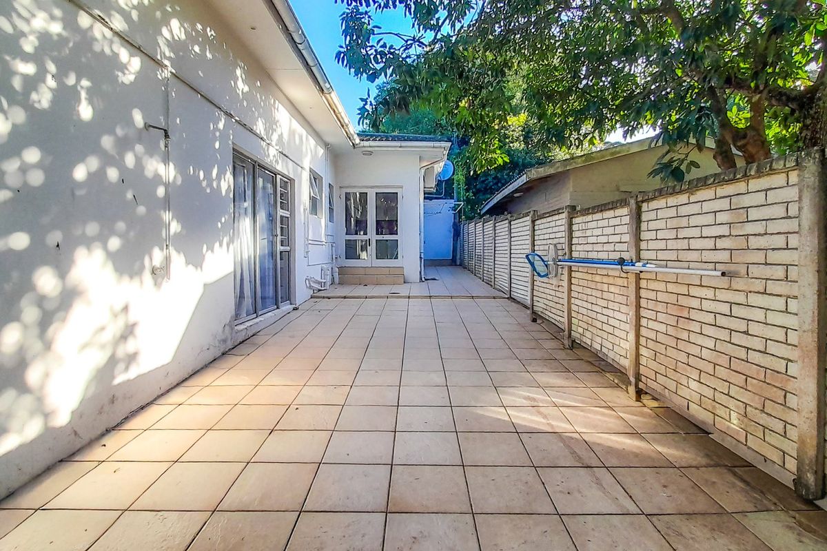A paved rear patio area featuring a brick boundary wall, sliding glass doors, and access to the main dwelling.