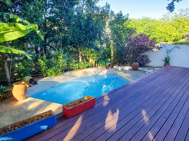 Outdoor pool area featuring a swimming pool, concrete surround, and timber decking, set within a private garden with established trees and boundary walls.