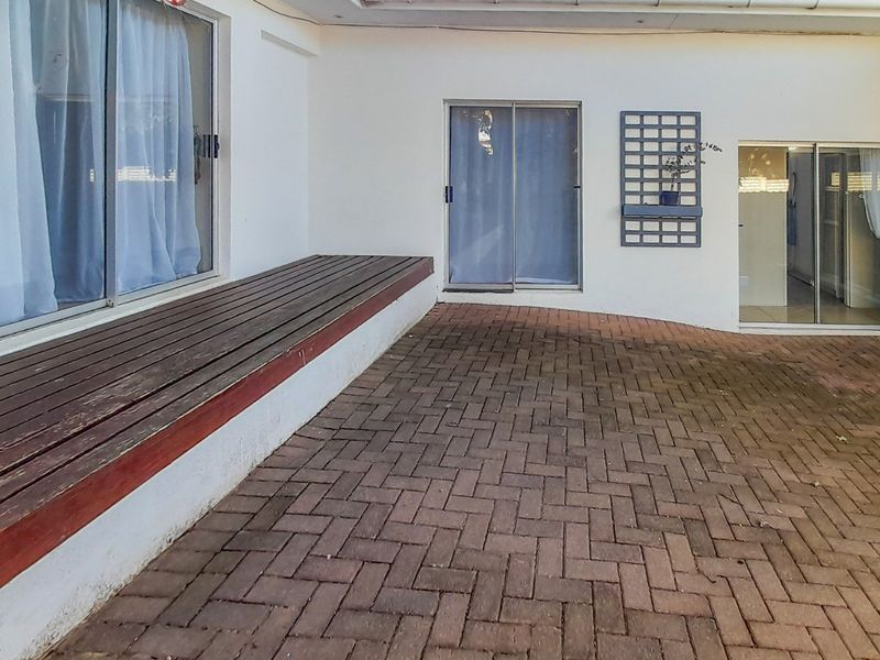 A covered outdoor patio area featuring paved flooring and a built-in timber deck, providing direct access to the home through multiple sliding glass doors.
