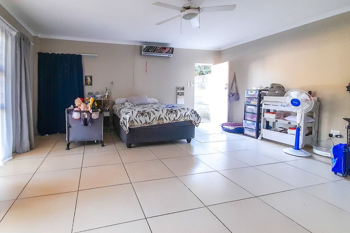Spacious bedroom featuring tiled flooring, a ceiling fan, and a wall-mounted air conditioning unit with direct access to the exterior.