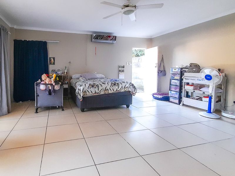 Spacious bedroom featuring tiled flooring, a ceiling fan, and a wall-mounted air conditioning unit with direct access to the exterior.