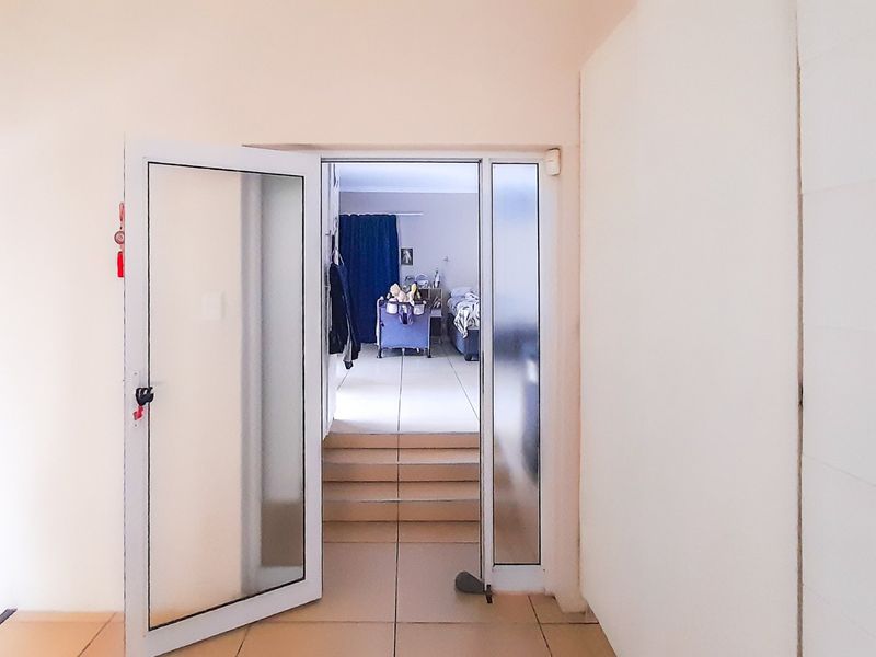 A transition hallway featuring tiled flooring and an aluminium framed glass door leading to an adjacent room with internal steps.