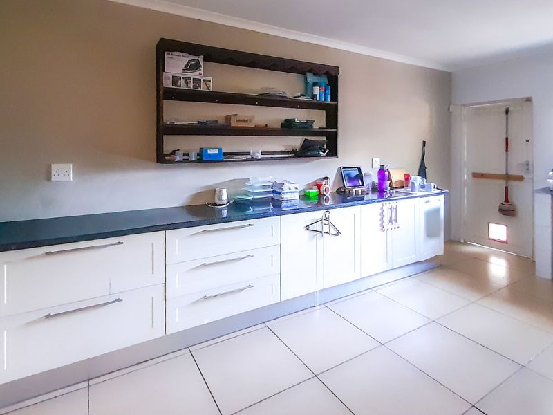 A functional laundry room featuring white built-in cabinetry, dark stone countertops, tiled flooring, and a convenient pet door.