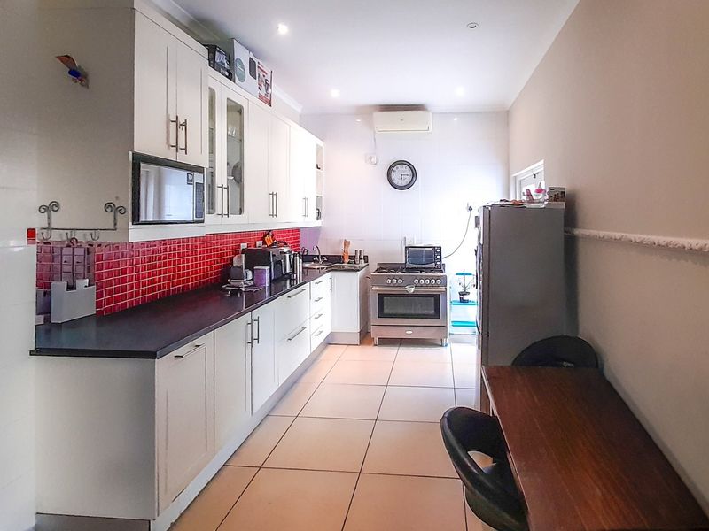 A functional kitchen featuring white cabinetry, a vibrant red tiled backsplash, dark countertops, and a built-in gas stove with oven.