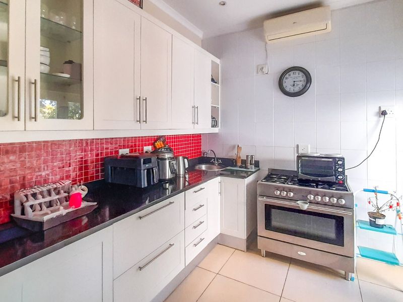 A functional kitchen featuring white cabinetry, dark granite countertops, a red tiled backsplash, and a stainless steel freestanding oven.