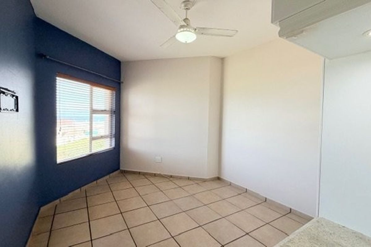 An empty bedroom featuring tiled flooring, a ceiling fan, and a window with blinds, offering a clean and neutral space ready for personalization.