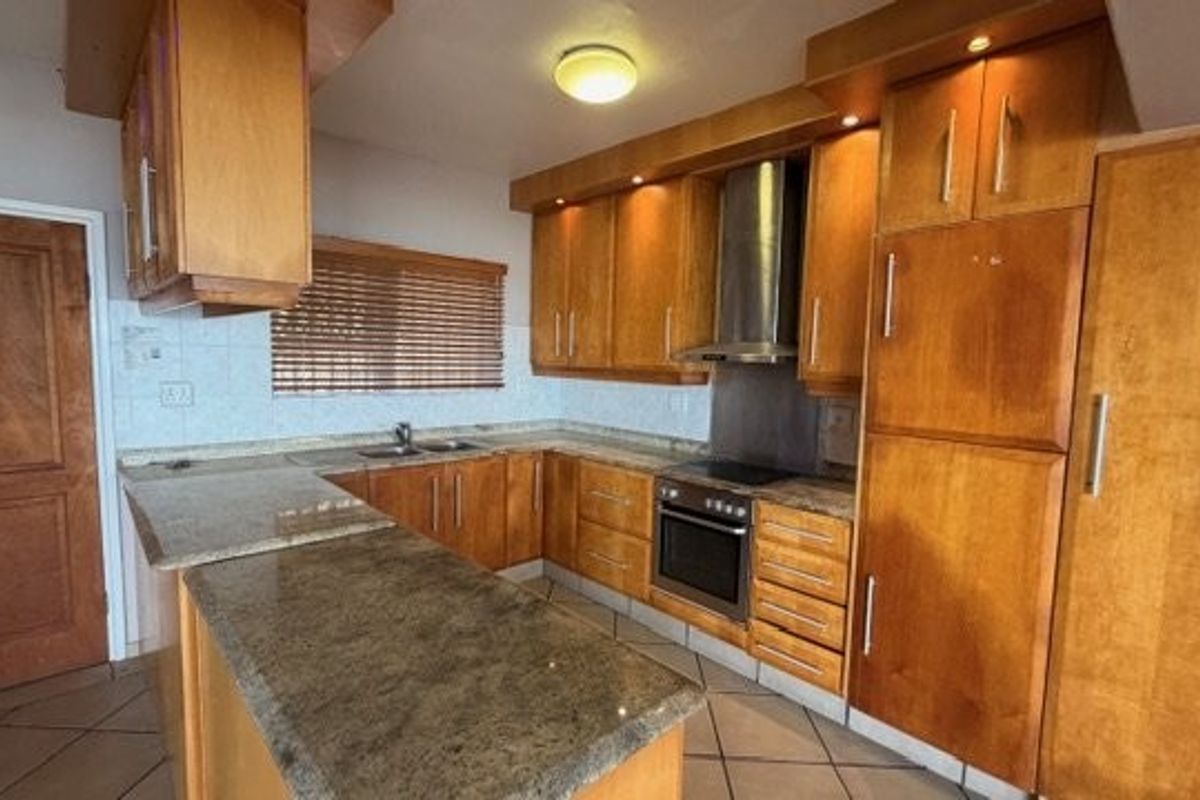 A functional kitchen featuring wooden cabinetry, stone countertops, built-in oven, extractor fan, and tiled flooring.