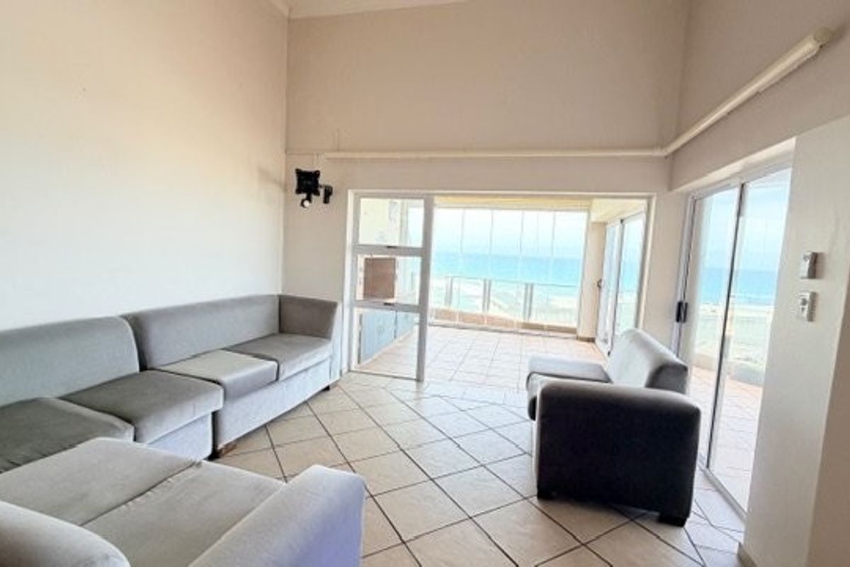 Spacious living area featuring tiled flooring, high ceilings, and large sliding glass doors leading to an enclosed balcony with ocean views.