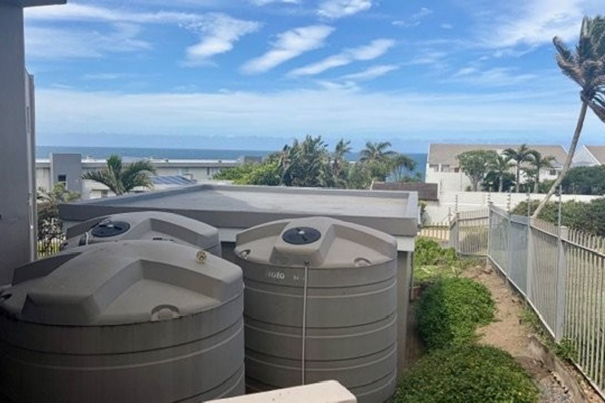 Rear exterior area featuring large water storage tanks, metal perimeter fencing, and a view towards the ocean.