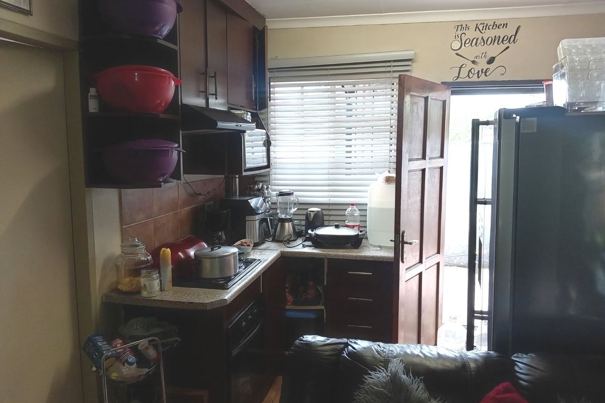 A compact kitchen featuring dark wood cabinetry, tiled splashbacks, and a built-in extractor fan, with direct access to the exterior.