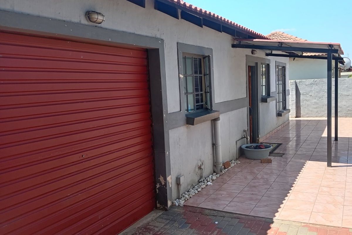 Exterior view of the property featuring a red roller garage door, tiled patio area, and paved driveway.