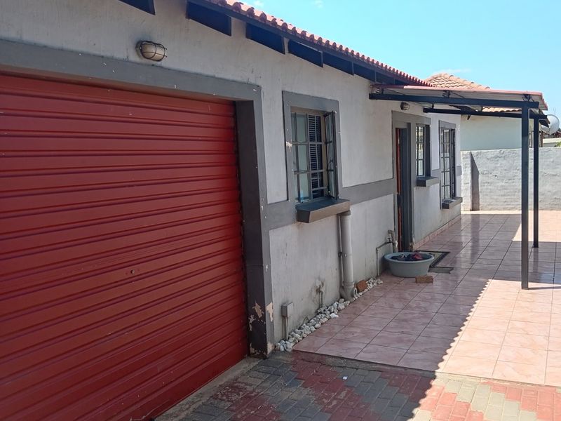 Exterior view of the property featuring a red roller garage door, tiled patio area, and paved driveway.