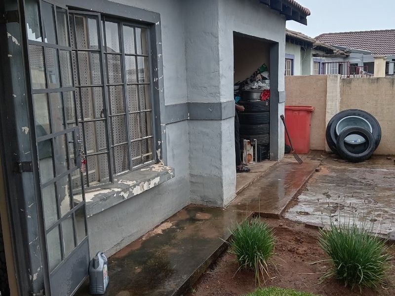 Exterior view of the property showing a side entrance, tiled roof, and paved area with a small garden patch.