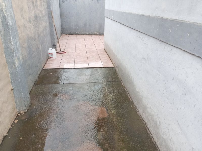 A narrow side passage or utility area featuring a mix of concrete and tiled flooring between two exterior walls.