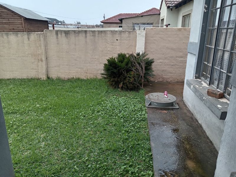 A view of the rear garden area featuring a lawn, perimeter boundary wall, and a concrete pathway adjacent to the house structure.