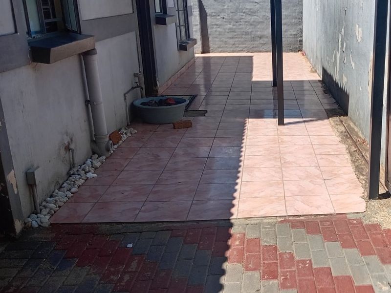 A paved side patio area featuring a covered walkway, tiled flooring, and a boundary wall, providing a functional outdoor space.