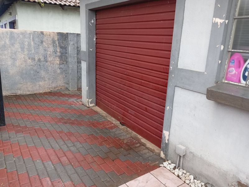 Exterior view of a garage featuring a red roller door, paved driveway, and surrounding boundary wall.