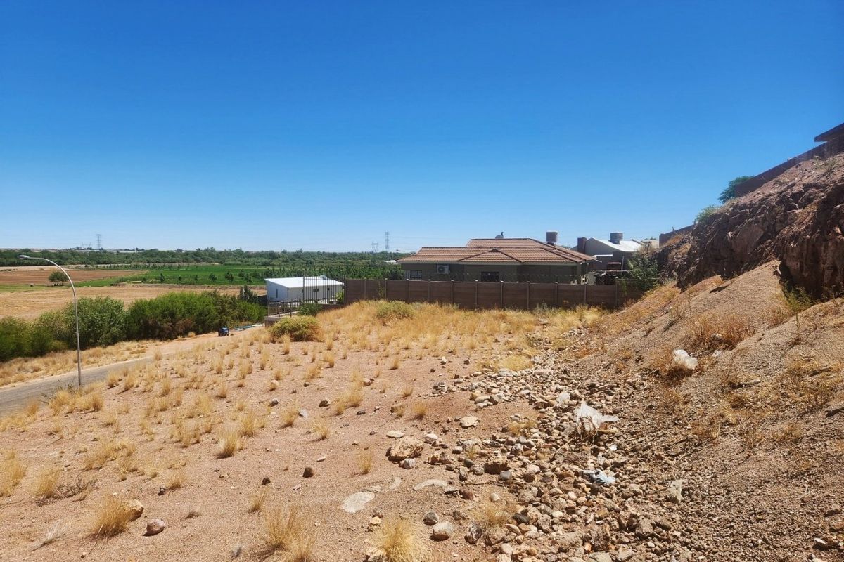 An elevated view of an unimproved residential plot featuring rocky terrain, natural vegetation, and a surrounding precast concrete boundary wall.