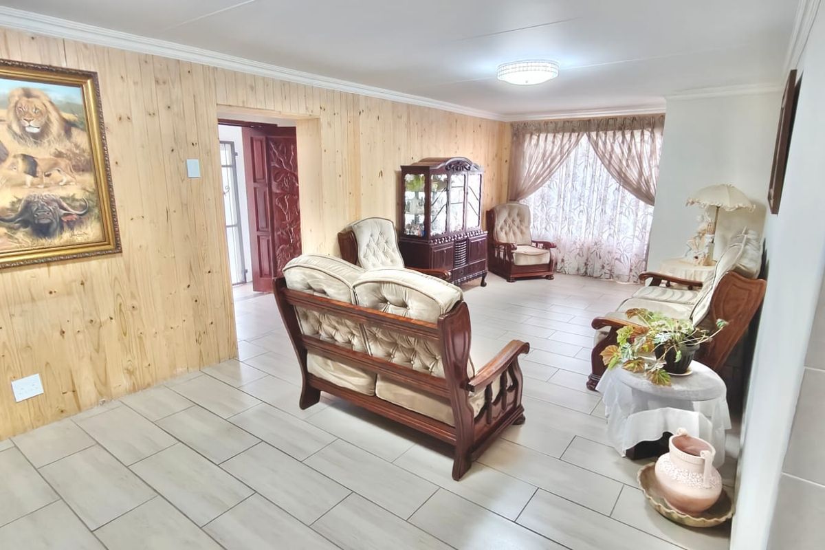 A spacious living room featuring light wood paneling, neutral tiled flooring, and a classic layout with access to an adjoining room.