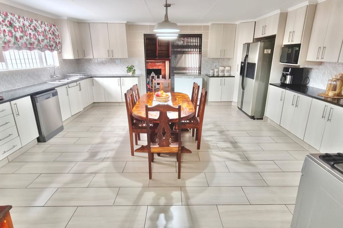 Spacious kitchen featuring extensive built-in cabinetry, light-toned tiled flooring, and a central dining area with direct access to an adjacent room.
