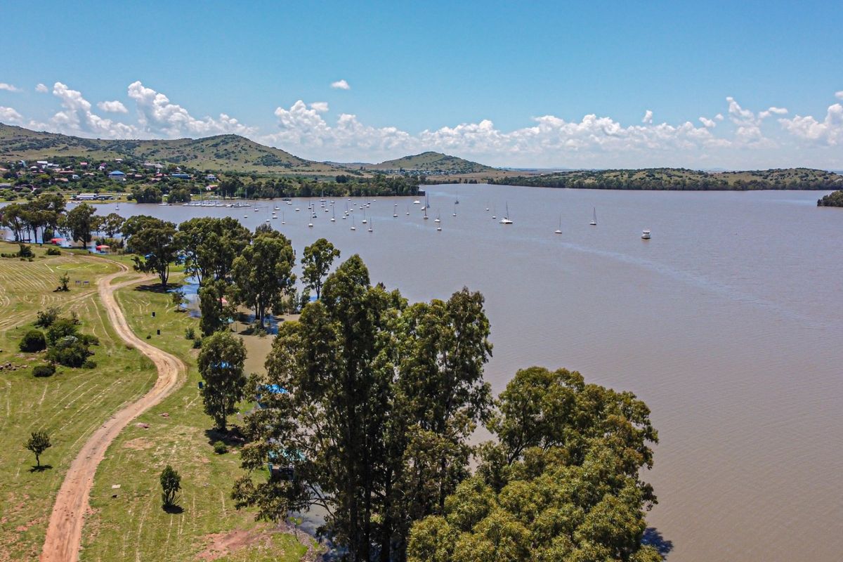 An aerial view of a large dam or lake with surrounding landscape, trees, and distant hills.